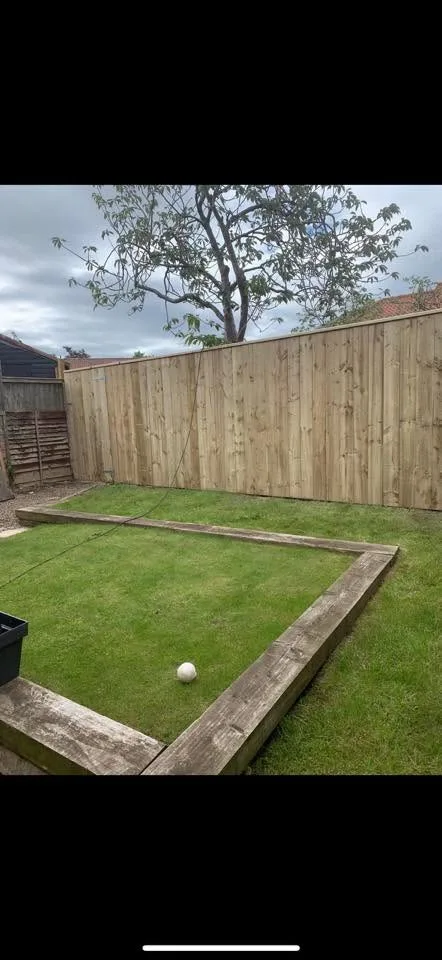 New timber fence with raised sleeper border around a freshly laid lawn
